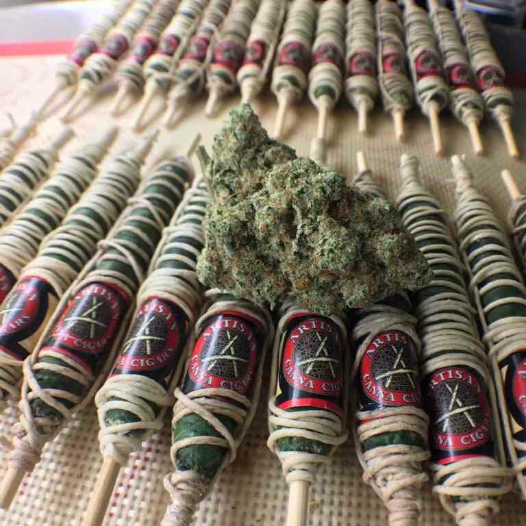 a pile of cannabis Thai Sticks rolled by Artisan Canna Cigars with a weed nugget sitting on top.